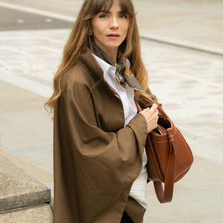 Woman wearing a black and beige houndstooth silk scarf with brown coat, white shirt on a city street.