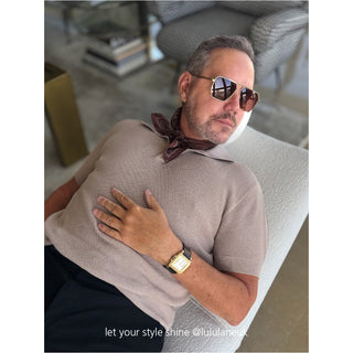 Men’s Indian red paisley silk neckerchief styled with a taupe knit polo and black trousers; relaxed luxury look with gold watch and sunglasses.