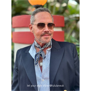 Navy silk square scarf featuring paisley print worn as a neckerchief with a blue shirt and navy blazer by a stylish man showcasing a polished and classic semi-formal look.
