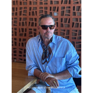 Stylish black and blue paisley silk neckerchief worn with light blue striped shirt against rustic wooden backdrop