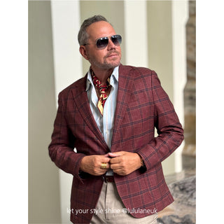 Stylish man wearing burgundy plaid blazer with red, black and beige geometric silk neckerchief, white shirt, and sunglasses for elegant semi formal look