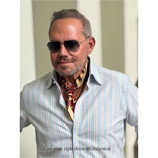 Stylish man wearing red, black and beige geometric silk square scarf as a neckerchief with light blue striped shirt and aviator sunglasses