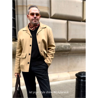 Stylish man wearing a red, black and beige geometric Kanagawa wave silk scarf with camel coat, black sweater and trousers against stone building backdrop