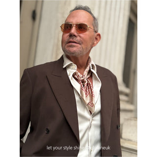 Men’s silk neckerchief featuring a beige horseshoe print, styled under the collar of a dark brown suit. The elegant silk scarf adds a refined touch to a dapper city look.