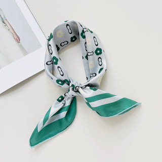 Folded teal green silk scarf with light grey base featuring green floral patterns and chain links, tied elegantly with striped edges