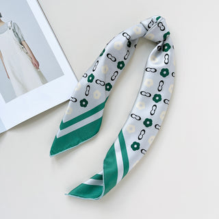 Folded square silk scarf with light grey base, teal green borders and decorative pattern of green flowers and chain links throughout