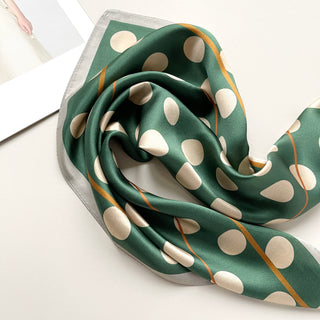 Jade green silk scarf with beige polka dots and gold trim, elegantly draped to showcase its luxurious sheen and square bandana design