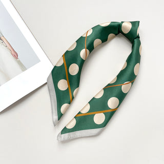 Jade green silk scarf with light beige polka dots and gold accent stripes, folded in a triangle shape with silver-gray trim on a white background