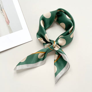 Jade green silk scarf with beige polka dots tied in a casual neckerchief style, showcasing its shiny fabric and retro pattern