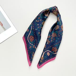 Navy blue silk scarf with vintage floral pattern featuring ornate red and gold blooms, green foliage, and pink border trim on white background