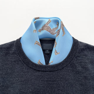Sky blue silk scarf with leopard pattern styled around neck of gray sweater, showing luxurious twill texture and playful design accent