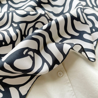 Silk scarf with charcoal grey abstract rose pattern on white background, showing luxurious fabric texture and hand-rolled edge
