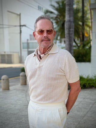 Men’s silk neckerchief featuring a beige horseshoe print, styled under the collar of a cream white polo shirt. The elegant silk scarf adds a refined touch to a dapper city look.
