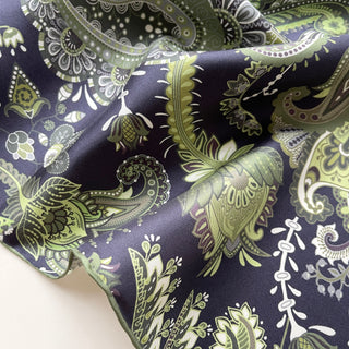 Luxurious silk scarf with intricate paisley pattern in forest green, navy, and white, showcasing the shimmering fabric texture and hand-rolled edges