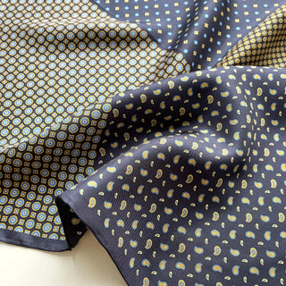 Navy blue silk scarf featuring a patchwork of geometric circles, dots, and paisley patterns in gold, blue and white with hand-rolled edges