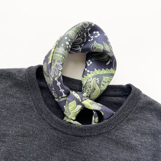 Forest green paisley silk scarf with navy background tied around collar of dark gray sweater, showing intricate pattern and hand-rolled edge