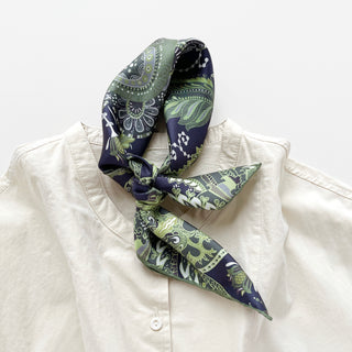 Forest green and navy silk scarf with intricate paisley pattern, tied elegantly at the collar of a cream button-up shirt, showcasing hand-rolled edges