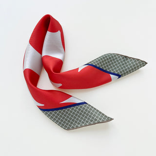 Orangey-red silk scarf with white geometric pattern and deep green checkered ends, displayed in flowing S-shape against white background