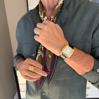Men’s silk and cotton neck scarf in olive with stylised bird print, styled with a dark green jacket.