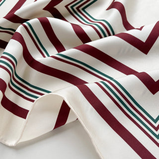 Luxurious silk scarf with modern geometric pattern featuring burgundy and green lines on cream white background, showing smooth twill texture