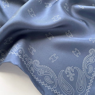 Dusty blue silk scarf featuring delicate white dotted paisley pattern and MARVEL logo designs on luxurious twill fabric with subtle sheen