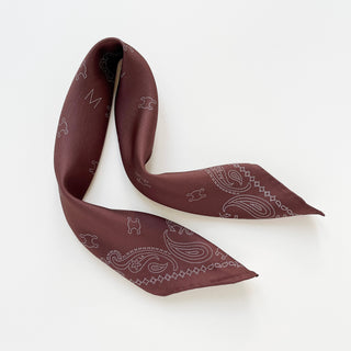 Indian red silk neckerchief with dotted paisley pattern and MARVEL logo, elegantly arranged showing silky texture and hand-rolled edges