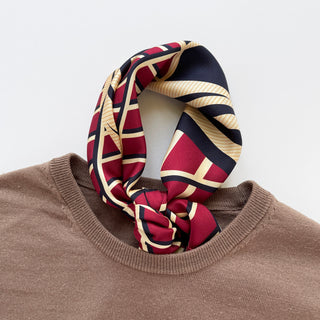 Luxury geometric Kanagawa Wave silk scarf in red, navy and gold, artfully tied around the collar of a brown sweater showing its double-sided pattern