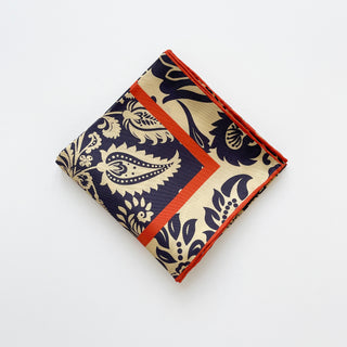 Folded navy and beige silk scarf with intricate paisley pattern and vibrant orange border, featuring hand-rolled edges and luxurious twill texture