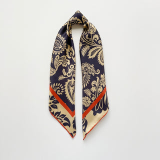 Luxurious navy and beige silk scarf with intricate paisley pattern, featuring hand-rolled edges and bold orange border, displayed in elegant square format.