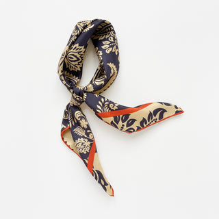 Luxurious navy and beige silk scarf with elegant paisley pattern, styled in a loose knot displaying its shiny twill texture and vibrant orange border