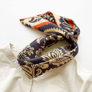 Elegant navy and beige silk scarf with intricate paisley pattern and orange border, styled in a knot over light clothing showing hand-rolled edges