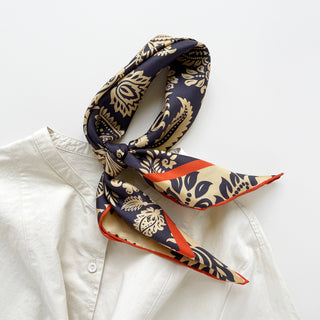Navy and beige paisley silk scarf with orange border, elegantly knotted and styled on white shirt collar, showcasing luxurious sheen and hand-rolled edges