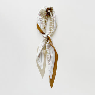 Elegant silk scarf in beige and white with monogram pattern, featuring striped design and mustard border, tied in a stylish knot against neutral background