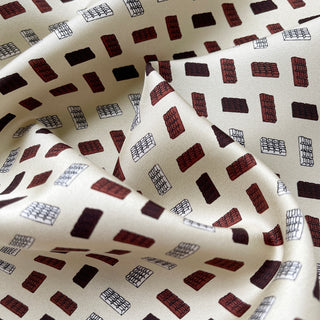 Ivory silk scarf with geometric block pattern in burgundy and black, showing luxurious twill texture with elegant draping folds