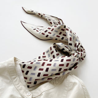 Ivory silk scarf with geometric burgundy and navy block pattern, elegantly tied with hand-rolled edges, displayed on a white button-up collar