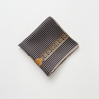 Folded silk scarf with black and beige houndstooth pattern, featuring decorative gold chain design on one edge, shown on white background