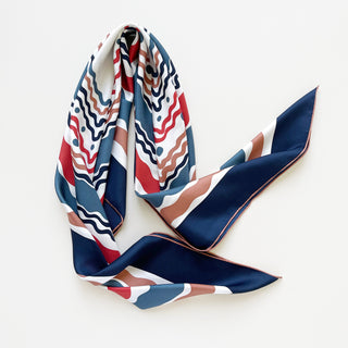 Luxury silk scarf with wavy pattern in navy blue, red, and earth tones, featuring hand-rolled edges and glossy twill fabric