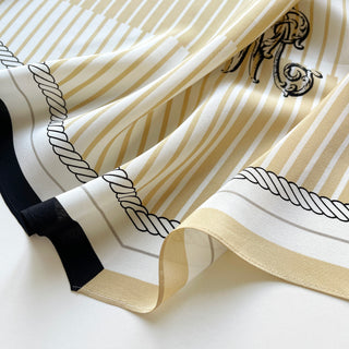 Pale yellow and beige silk scarf with elegant striped pattern, decorative monogram accent, and rope design details, featuring black trim