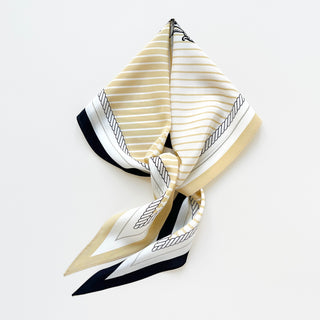 Elegant silk scarf in beige and white stripes with black accents, featuring decorative rope pattern borders and monogram design, displayed folded.
