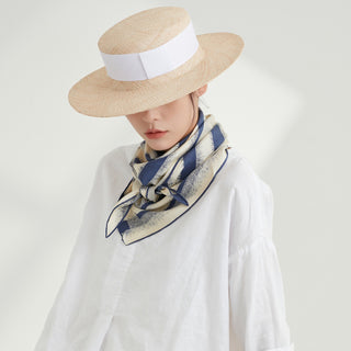 Luxury striped silk scarf in blue and cream worn as a neckerchief with a straw boater hat and white blouse, showcasing elegant drape and texture