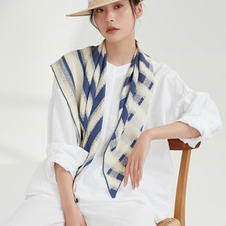 Triangle silk scarf with blue and cream striped pattern draped over white outfit, showcasing the scarf's soft texture and hand-rolled edges