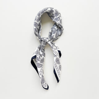 White silk bandana scarf with navy blue paisley pattern, elegantly knotted to display its square shape and dark border trim
