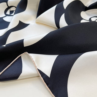 Luxurious black and white silk scarf featuring elegant camellia flower pattern, showing smooth twill fabric with hand-rolled edge and flowing folds.