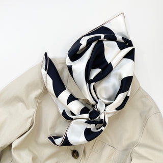 Black and white silk scarf with camellia flower pattern elegantly tied around the collar of a beige trench coat, showcasing its luxurious texture