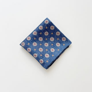 a luxury folded silk neckerchief with circular medallion pattern in denim blue with hand-rolled edges.