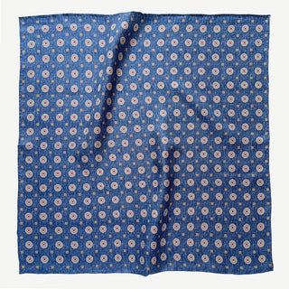 Denim blue silk neckerchief with repeating taupe medallion pattern, displayed flat showing hand-rolled edges and luxurious twill texture
