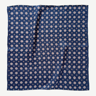 Dark denim blue silk neckerchief with repeating taupe medallion pattern, displayed flat showing hand-rolled edges and luxurious twill texture