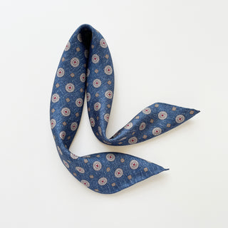 Denim blue silk neckerchief with taupe medallion pattern, elegantly folded to display its 53cm hand-rolled edges and classic design