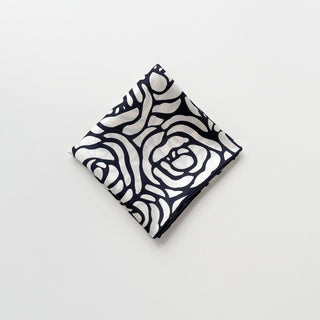 Folded women's silk square scarf with charcoal black abstract rose pattern on cream white background with hand-rolled edges.