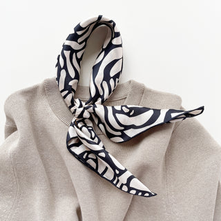 women's silk scarf with charcoal black abstract rose pattern on cream white background, elegantly knotted on a beige sweater